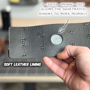 May include: Close-up of a gray leather watch band with a center opening for smartwatch sensors. The band has a soft leather lining and decorative stitching. Text on the image reads: "A CENTER OPENING THAT ALLOWS THE SMARTWATCH SENSORS TO WORK PROPERLY" and "SOFT LEATHER LINING".