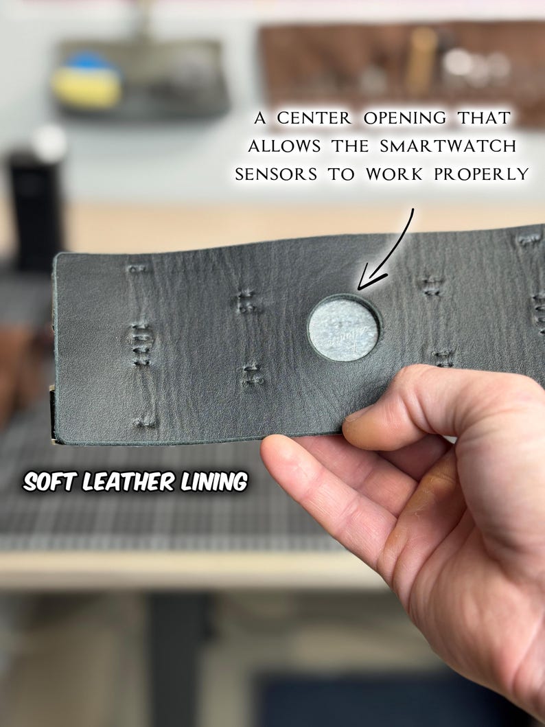 May include: Close-up of a gray leather watch band with a center opening for smartwatch sensors. The band has a soft leather lining and decorative stitching. Text on the image reads: "A CENTER OPENING THAT ALLOWS THE SMARTWATCH SENSORS TO WORK PROPERLY" and "SOFT LEATHER LINING".