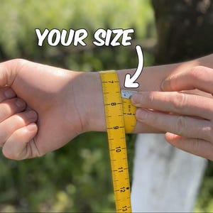 May include: A yellow measuring tape is wrapped around a wrist to measure its circumference. The text "YOUR SIZE" is above the wrist. The tape is marked in inches, with the measurement at approximately 7 inches.