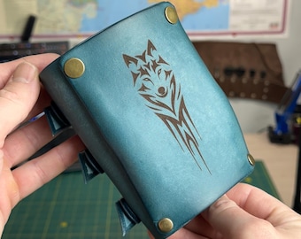 May include: Teal leather bracer with a wolf design. The bracer features a detailed wolf head and tribal-style accents. It is secured with brass rivets and straps, showcasing a rustic, handcrafted aesthetic.