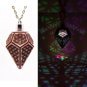Può includere: Una collana con un ciondolo in legno con un design geometrico. Il ciondolo ha la forma di un diamante e contiene una luce che proietta motivi colorati sul muro dietro di esso.