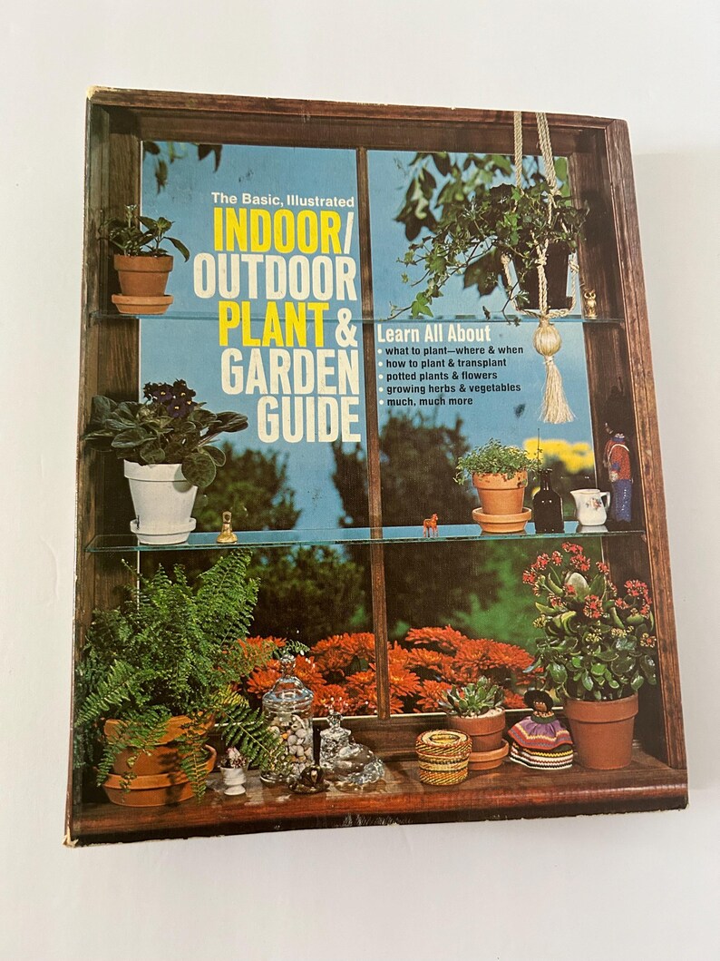 May include: A vintage wooden display case with glass shelves, filled with potted plants and decorative items. The case features a book titled "Indoor/Outdoor Plant & Garden Guide". The background shows a vibrant outdoor scene.