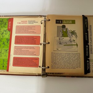 May include: Open vintage gardening book with colorful illustrations and text. The book is open to a page with a diagram and the text "First, Plan Your Garden on Paper." The book is bound with metal rings.