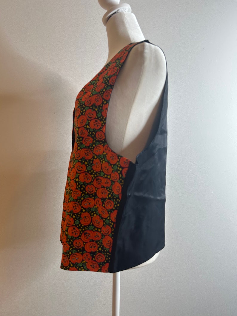 May include: A black sleeveless vest with a pumpkin print on the front. The vest is made of a soft, silky fabric and has a simple, classic design.