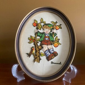 May include: Embroidered picture in a brown frame with a boy in a green shirt and red pants sitting in an apple tree with a bird. The picture is signed "Himmel".