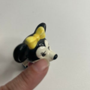 Może przedstawiać: Ceramiczna figurka czarno-białej myszy z kresk&oacute;wek z ż&oacute;łtą kokardką. Mysz ma białą twarz z czarnymi oczami i czarnym nosem.