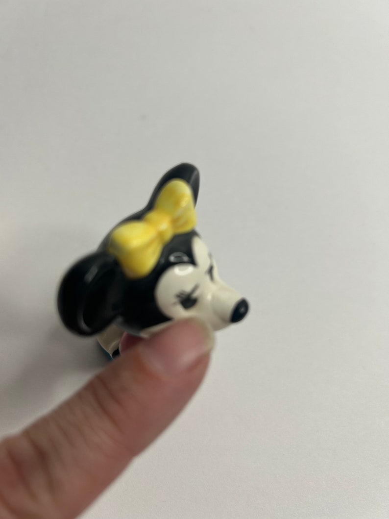 Może przedstawiać: Ceramiczna figurka czarno-białej myszy z kresk&oacute;wek z ż&oacute;łtą kokardką. Mysz ma białą twarz z czarnymi oczami i czarnym nosem.