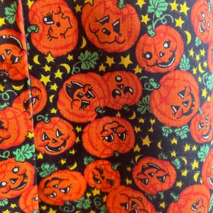 May include: Black fabric with a repeating pattern of orange jack-o'-lantern faces with black eyes and mouths. The background is filled with yellow stars and green leaves.