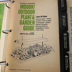 May include: An open book titled "The Basic, Illustrated Indoor/Outdoor Plant & Garden Guide" with a black and white illustration of plants under a light. The book's cover is tan with green text and black tabs.