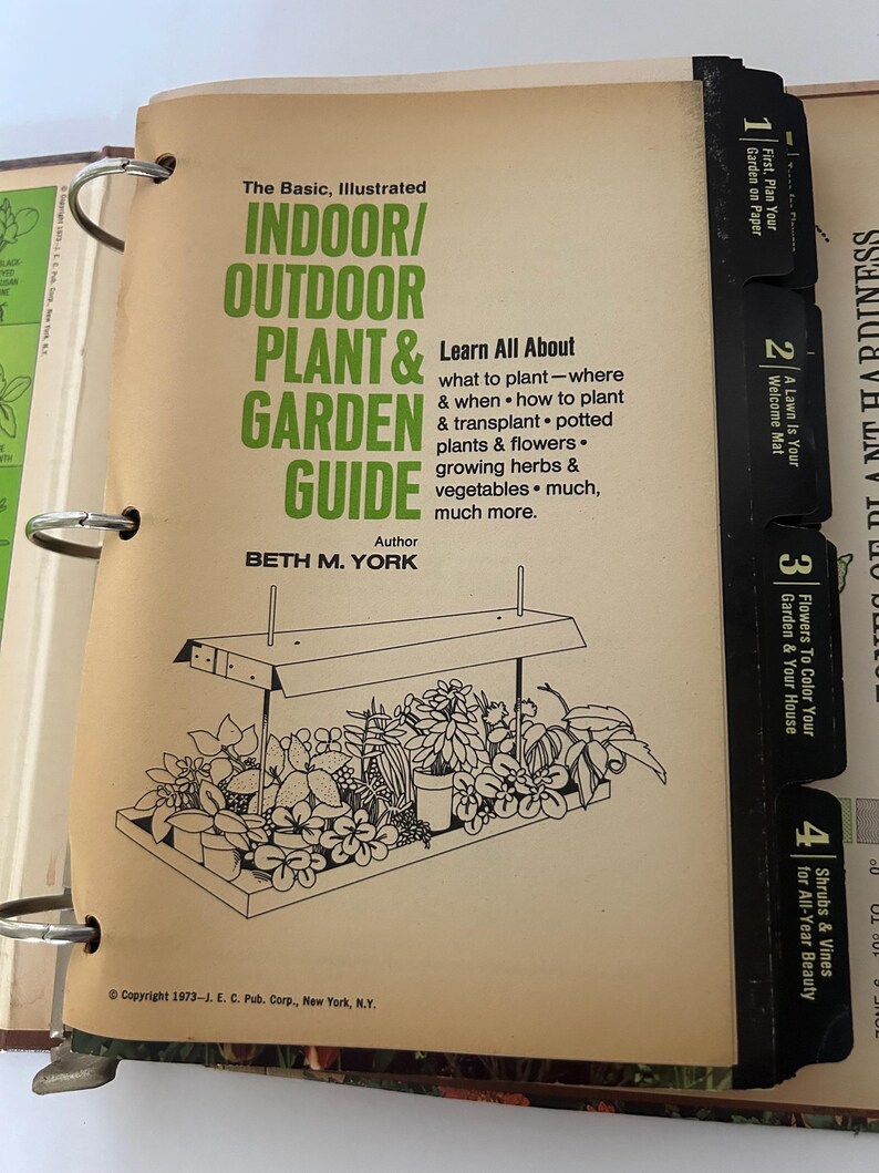 May include: An open book titled "The Basic, Illustrated Indoor/Outdoor Plant & Garden Guide" with a black and white illustration of plants under a light. The book's cover is tan with green text and black tabs.