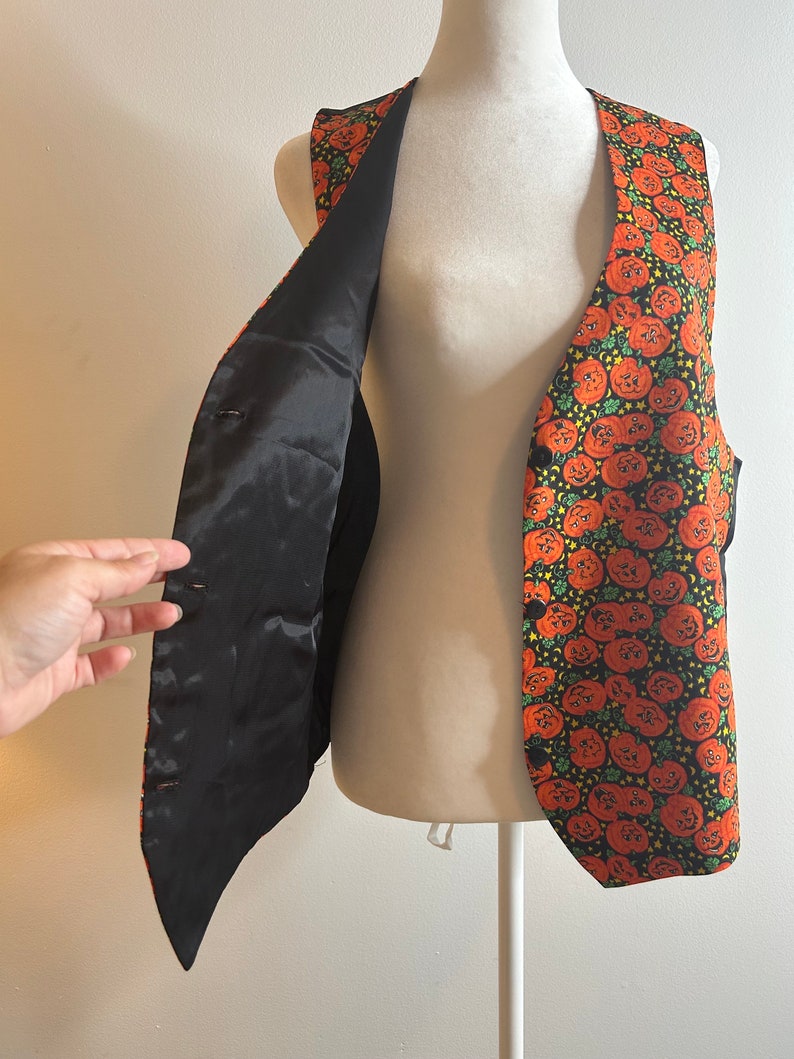 May include: A black vest with a pumpkin print. The vest has a black satin lining and is unbuttoned, showing the lining.