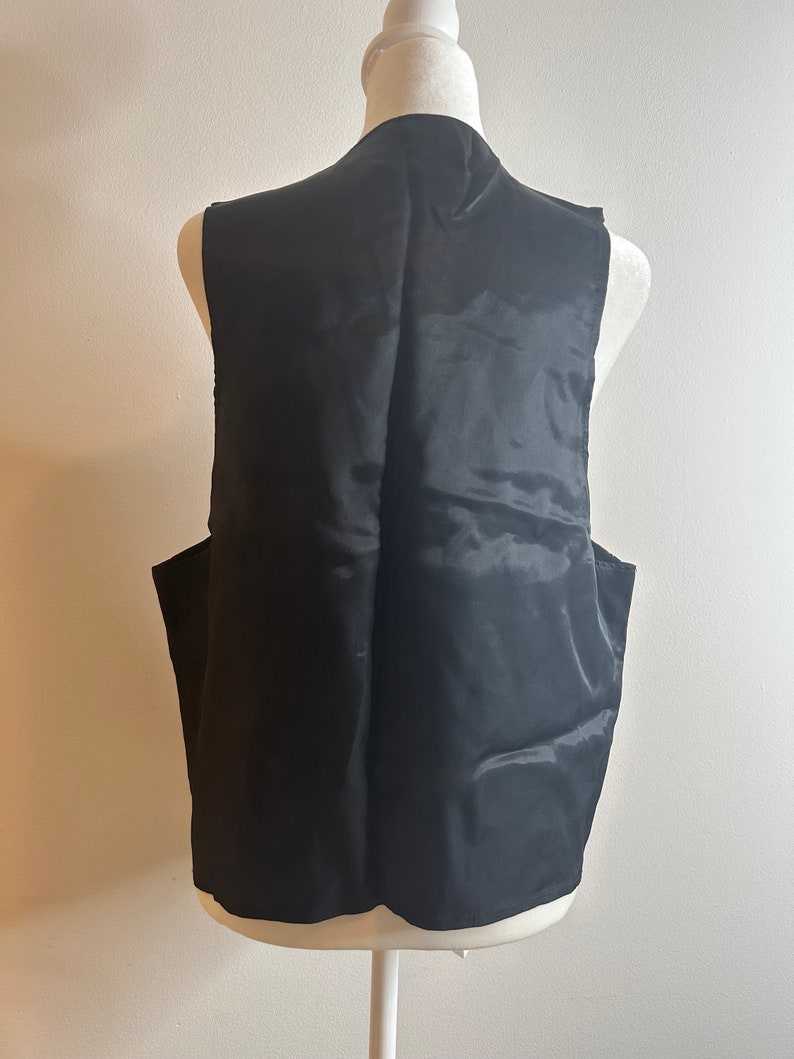 May include: A black sleeveless vest with a smooth, satin-like finish. The vest is displayed on a white mannequin.