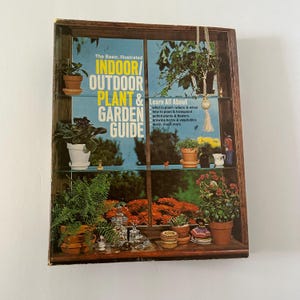 May include: A vintage book titled "The Basic, Illustrated Indoor/Outdoor Plant & Garden Guide." The cover features a window display with various potted plants and the text "Learn All About." The book is housed in a wooden frame.