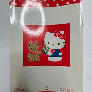 May include: A red and white book with a Hello Kitty and a bear character on the cover. The book has 32 pages and 17 stickers. The text on the back of the book reads "17 stickers, 32 pages, 発売元 株式会社サンリオ, MADE IN JAPAN, 180 97516-8 1.50, &copy;1976.1993 SANRIO CO., LTD."