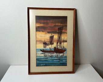 May include: A framed watercolor painting of a brown sailboat with sails and multiple people on board, sailing on a blue body of water with a sunset in the background.