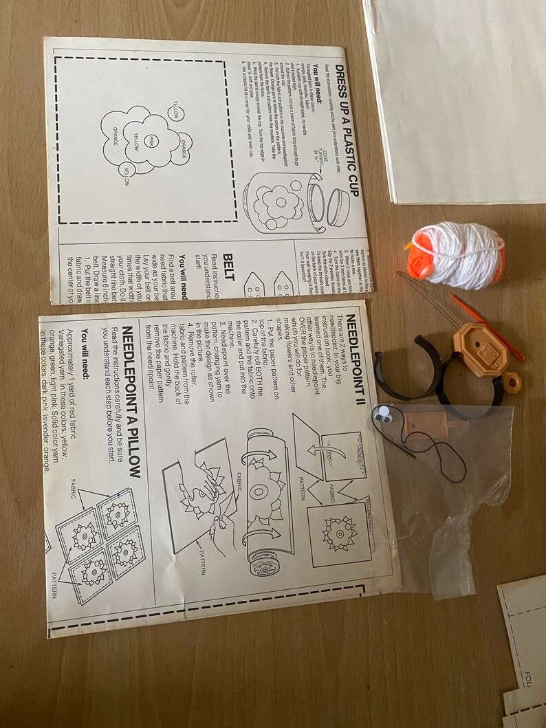 May include: A craft kit for making a needlepoint pillow. The kit includes a needlepoint canvas, yarn in various colors, a needlepoint tool, and instructions. The instructions show how to create a flower design.