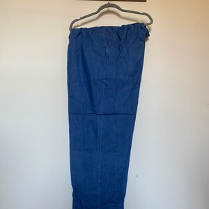 May include: A pair of blue denim pants hanging on a hanger. The pants have a wide leg and a relaxed fit.