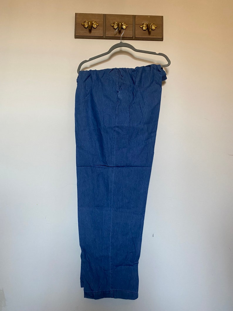 May include: A pair of blue denim pants hanging on a hanger. The pants have a wide leg and a relaxed fit.
