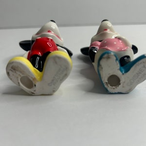 Może przedstawiać: Para ceramicznych figurek Mickey Mouse'a i Minnie Mouse. Mickey ma na sobie czerwone spodenki i ż&oacute;łte buty. Minnie ma na sobie r&oacute;żową sukienkę w białe kropki i niebieskie buty. Obie figurki mają napis "Disney Japan" na spodzie st&oacute;p.
