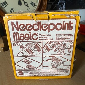 May include: A yellow box with the words "Needlepoint Magic" in brown letters. The box shows a toy machine that makes needlepoint designs. The text on the box says "The amazing new way to do needlepoint!" and "Make needlepoint designs in minutes!"  The box is from Mattel.
