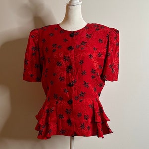 May include: A red blouse with a black floral pattern and a ruffled hem. The blouse has a button-up front and short sleeves.