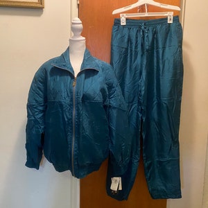 May include: A teal blue tracksuit with a zippered jacket and matching pants. The jacket has a stand-up collar and a zipper closure. The pants have an elastic waistband and a drawstring.