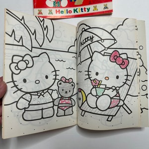 May include: A coloring book featuring Hello Kitty on the cover. The inside pages show two black and white illustrations of Hello Kitty, one with a beach umbrella and the other with a friend.
