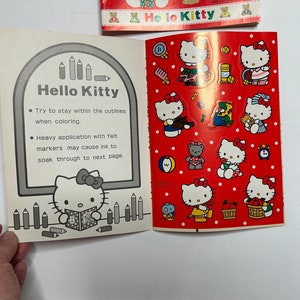 May include: A coloring book featuring Hello Kitty. The cover is red with white polka dots and features Hello Kitty in various poses. The inside of the book has a black and white illustration of Hello Kitty and instructions for coloring. The text reads "Try to stay within the outlines when coloring. Heavy application with felt markers may cause ink to soak through to next page."
