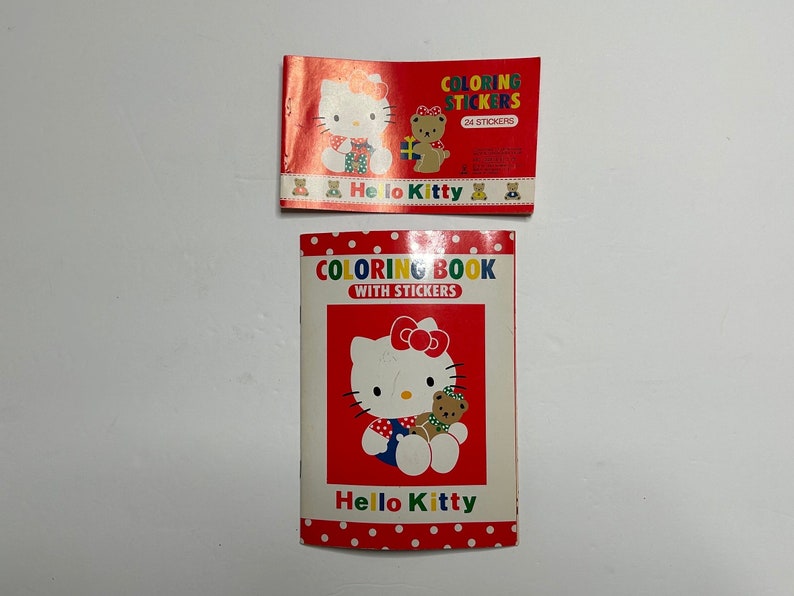 May include: Two Hello Kitty coloring books. The top book is red with white polka dots and says "Coloring Stickers" with 24 stickers. The bottom book is red with white polka dots and says "Coloring Book with Stickers". Both books feature Hello Kitty and a bear.