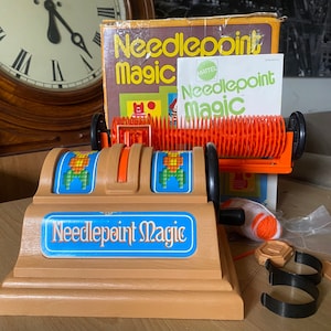 May include: A vintage Mattel Needlepoint Magic toy kit. The kit includes a plastic loom, yarn, needles, and instructions. The box features a colorful design with the text "Needlepoint Magic" and the Mattel logo.
