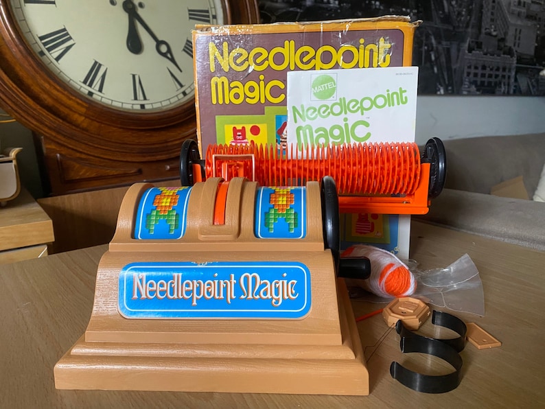 May include: A vintage Mattel Needlepoint Magic toy kit. The kit includes a plastic loom, yarn, needles, and instructions. The box features a colorful design with the text "Needlepoint Magic" and the Mattel logo.