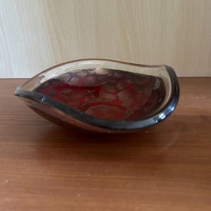 May include: A clear glass bowl with a red and gold interior. The bowl has a unique, curved shape with a black rim. The interior features a textured pattern, adding visual interest to this decorative piece.