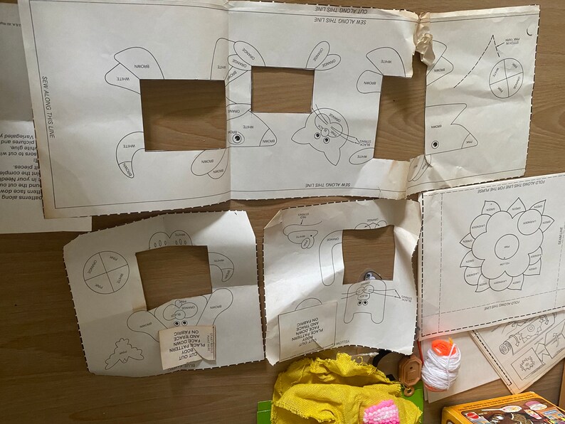 May include: A set of sewing patterns for creating various stuffed animals. The patterns include a flower, a bunny, a fish, and a crab. The patterns are printed on white paper with black lines.