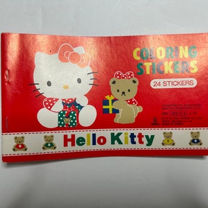 May include: A red and white coloring book with Hello Kitty and a bear holding a gift. The book has 24 stickers and is made in Taiwan. The text on the cover reads "Coloring Stickers" and "Hello Kitty".