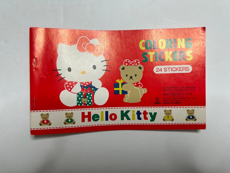 May include: A red and white coloring book with Hello Kitty and a bear holding a gift. The book has 24 stickers and is made in Taiwan. The text on the cover reads "Coloring Stickers" and "Hello Kitty".