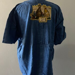 May include: A blue denim shirt with a patch on the back featuring two cats sitting by a fence with the text "Honey, Good Sale".