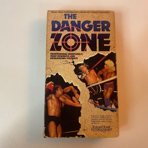 May include: A VHS tape with a yellowed cover featuring a wrestling match. The title "The Danger Zone" is in large, bold, black letters with a red target symbol. The text "Professional Wrestling's Most Powerful and Devastating Moments" is below the title. The tape is from Turner Home Entertainment.