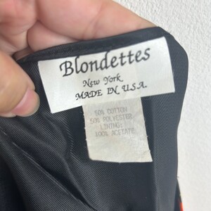 May include: A white tag with black text that reads "Blondettes New York MADE IN USA."  The tag also includes the fabric content: "50% Cotton 50% Polyester Lining: 100% Acetate."