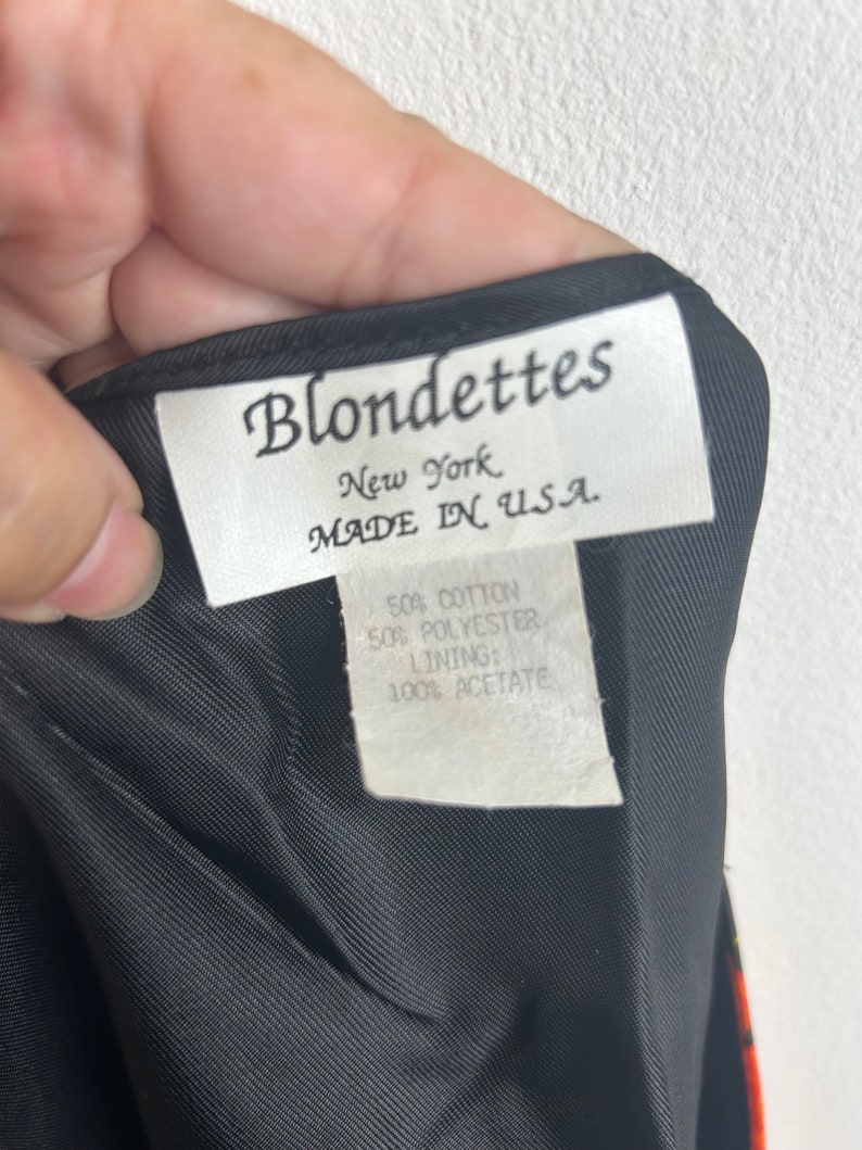 May include: A white tag with black text that reads "Blondettes New York MADE IN USA."  The tag also includes the fabric content: "50% Cotton 50% Polyester Lining: 100% Acetate."