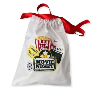 May include: White drawstring bag with a red ribbon. The bag has a movie night theme with a popcorn bucket, movie tickets, and a film reel. The text "Movie Night" is printed on the bag.