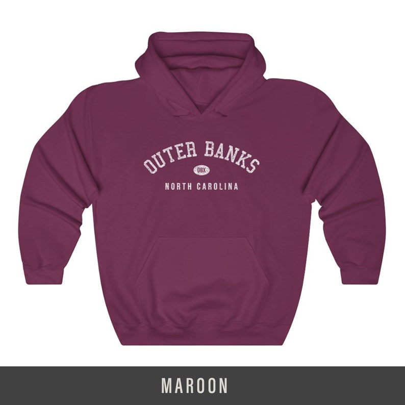 Puede incluir: Sudadera con capucha color granate con el texto "Outer Banks" en blanco, con un peque&ntilde;o c&iacute;rculo que contiene el texto "OBX" debajo. El texto "North Carolina" est&aacute; debajo del c&iacute;rculo.