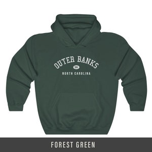 Puede incluir: Sudadera con capucha verde bosque con texto blanco que dice "Outer Banks" en un arco sobre un c&iacute;rculo con "OBX" dentro. Debajo del arco est&aacute; el texto "North Carolina".