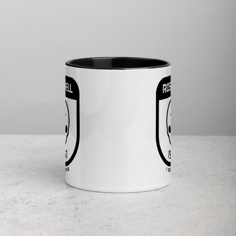 Pu&ograve; includere: Tazza da caff&egrave; in ceramica bianca con bordo e manico neri. La tazza presenta una grafica in bianco e nero di un UFO con il testo "Roswell" e "I Believe" su entrambi i lati.
