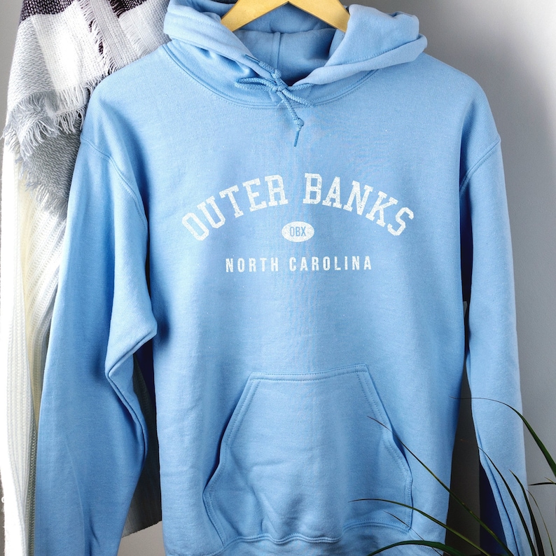 Puede incluir: Sudadera con capucha azul claro con texto blanco que dice "Outer Banks OBX North Carolina".