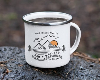 May include: White enamel camping mug with a black and orange mountain and sun design. The mug features the text "Wilderness Awaits" and the names "Sam + Whitney" with the date "9.26.20". The mug has a silver rim and a white handle.