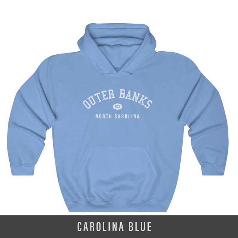 Puede incluir: Una sudadera con capucha azul cielo con el texto "Outer Banks" en blanco, con un peque&ntilde;o c&iacute;rculo que contiene el texto "OBX" debajo y el texto "North Carolina" debajo.