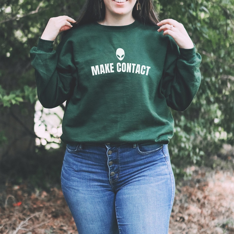 May include: A dark green sweatshirt with a white alien head graphic and the text "MAKE CONTACT" printed on the front.