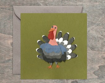 May include: A paper craft turkey with a blue, gray, and white patterned body and a pink head and beak on a green background.