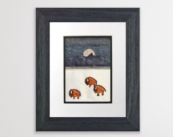 May include: Framed paper art with a collage of blue and gray paper depicting a mountain range and a full moon. Three brown paper bison are walking across a white paper background.