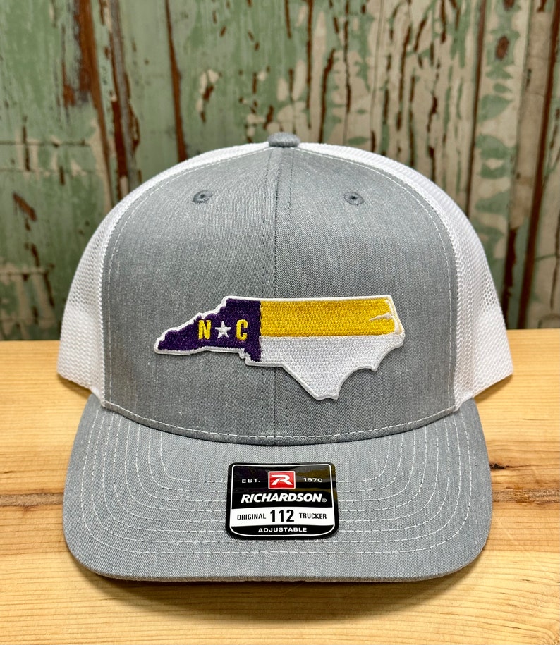 May include: Gray and white trucker hat with a North Carolina state outline patch in purple, yellow, and white. The patch has the letters "N*C" in purple. The hat has a black label with the text "Richardson" and "112" on it.